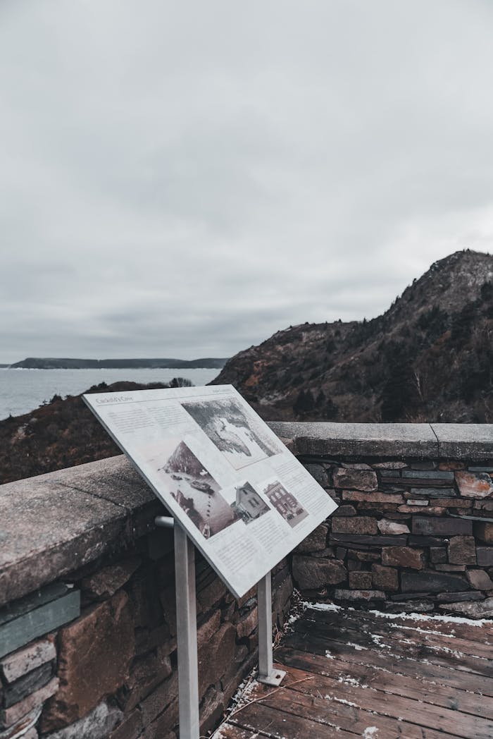 A historical sign at a scenic overlook with a view of hills and coastline.