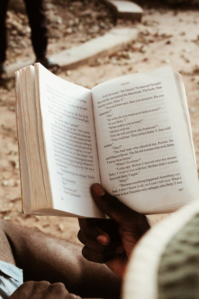 Person reading a book outside on a sunny day, capturing a moment of relaxation.
