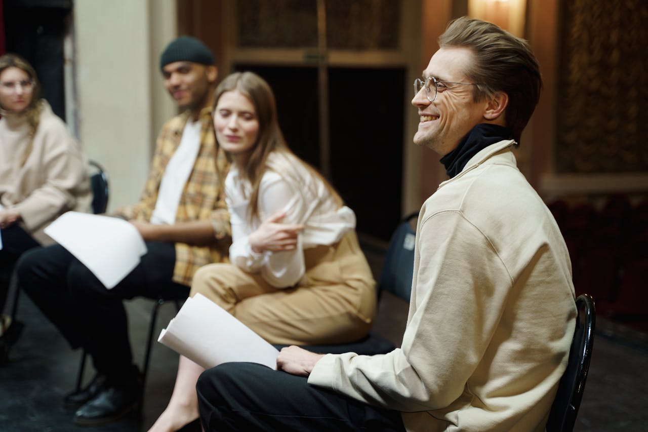 A group of actors smiles during a theater rehearsal session indoors.